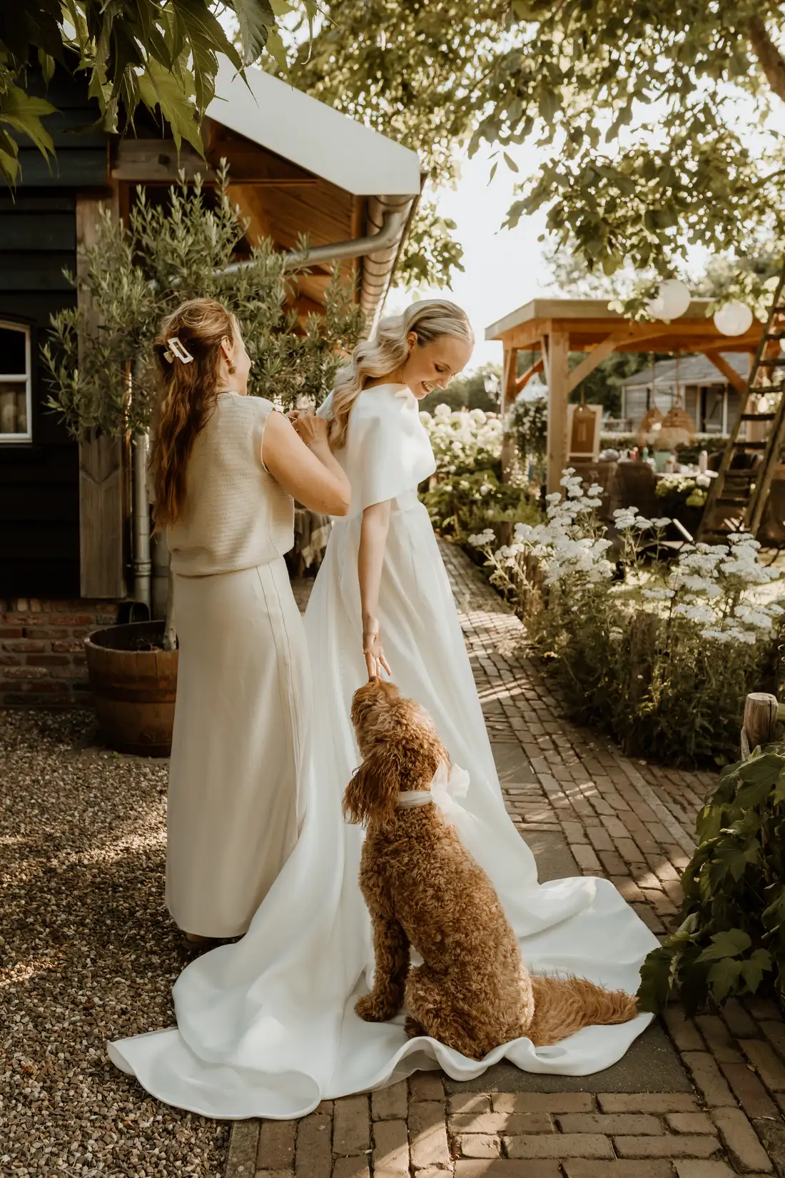 Bruid met bruidsmeisje en hond in de tuin op haar trouwdag